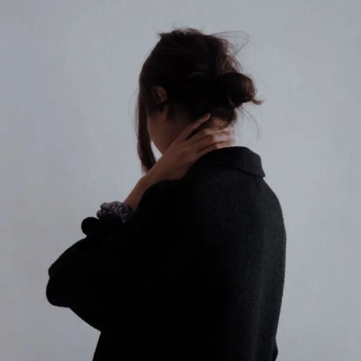 Person from behind reaching up to touch the back of their neck, suggesting tension and fatigue