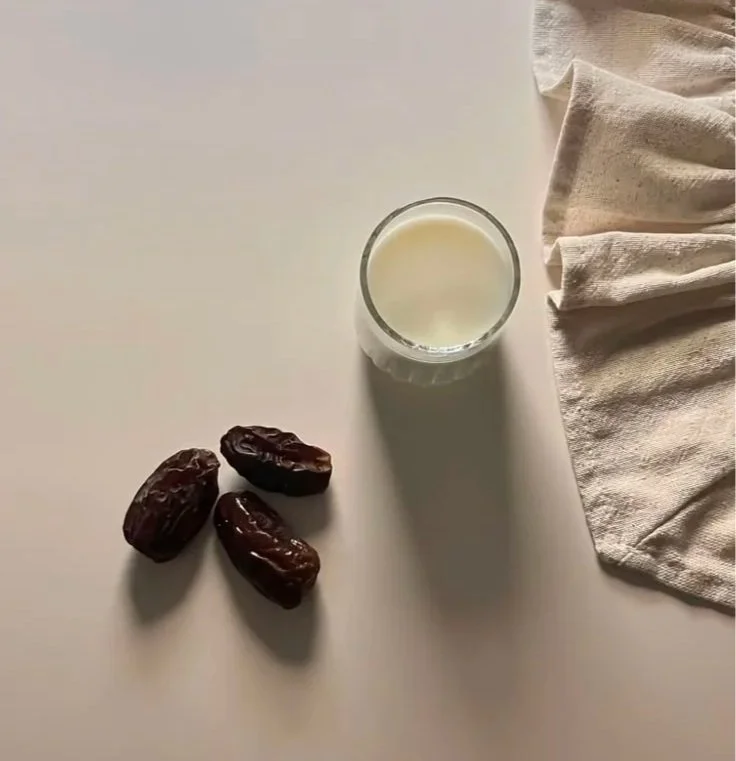 Dates and a glass of milk on a cream surface, a traditional gentle iftar pairing