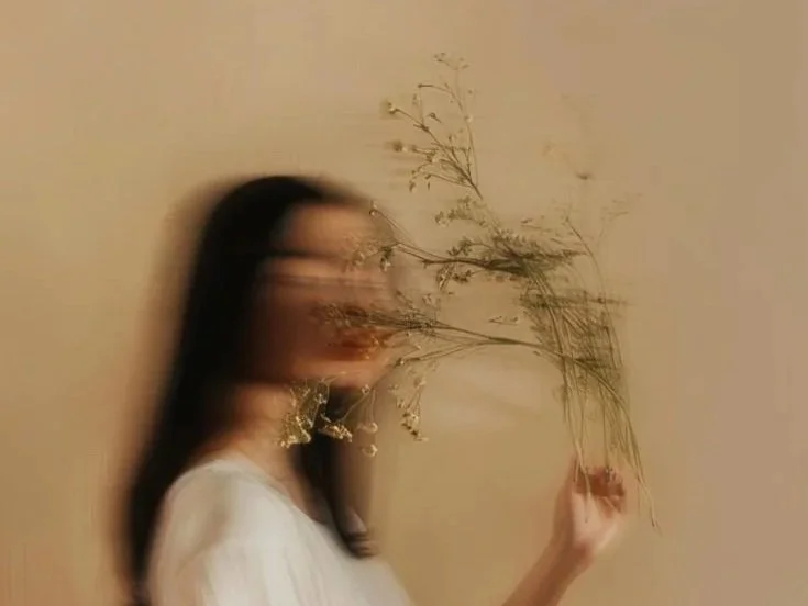 Soft motion-blur portrait of a woman holding dried flowers near her face