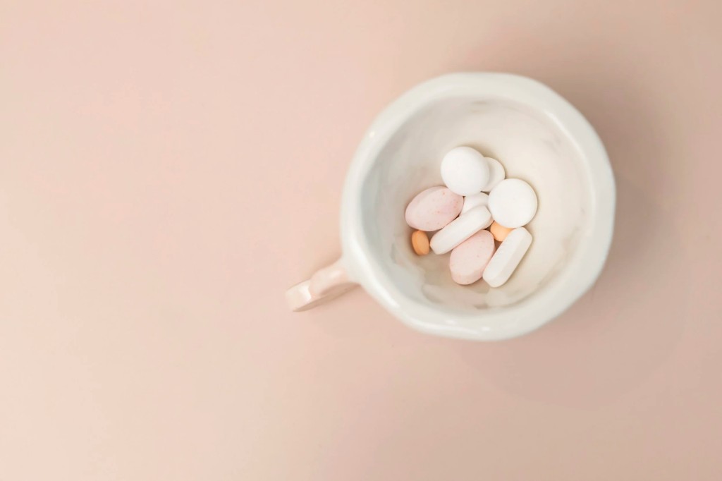 Ceramic cup with supplement pills and tablets on a soft peach background