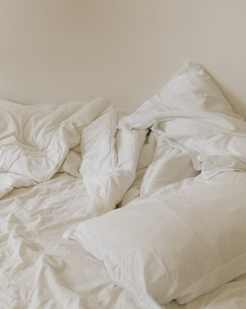 Unmade white bed with rumpled linens and pillows, evoking midday fatigue and rest